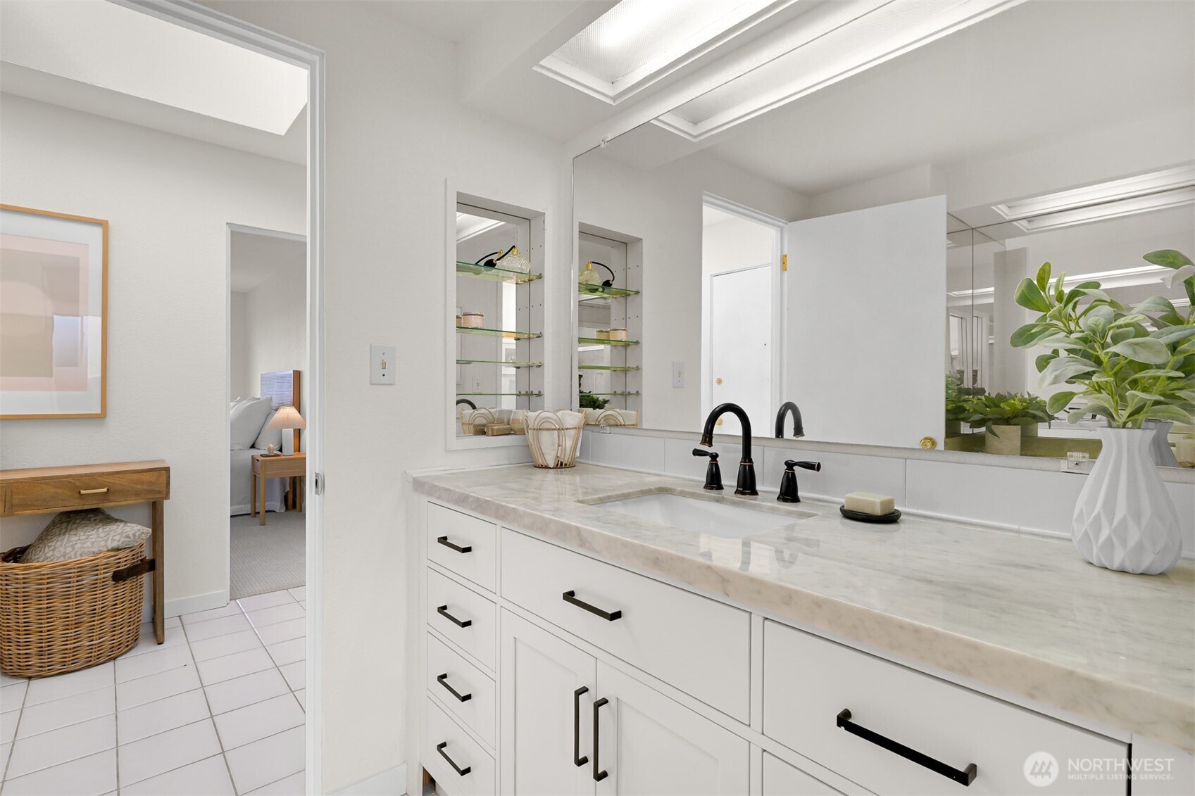 Bright bathroom with a marble-look vanity, black faucets, mirrored wall, and built-in glass shelves.