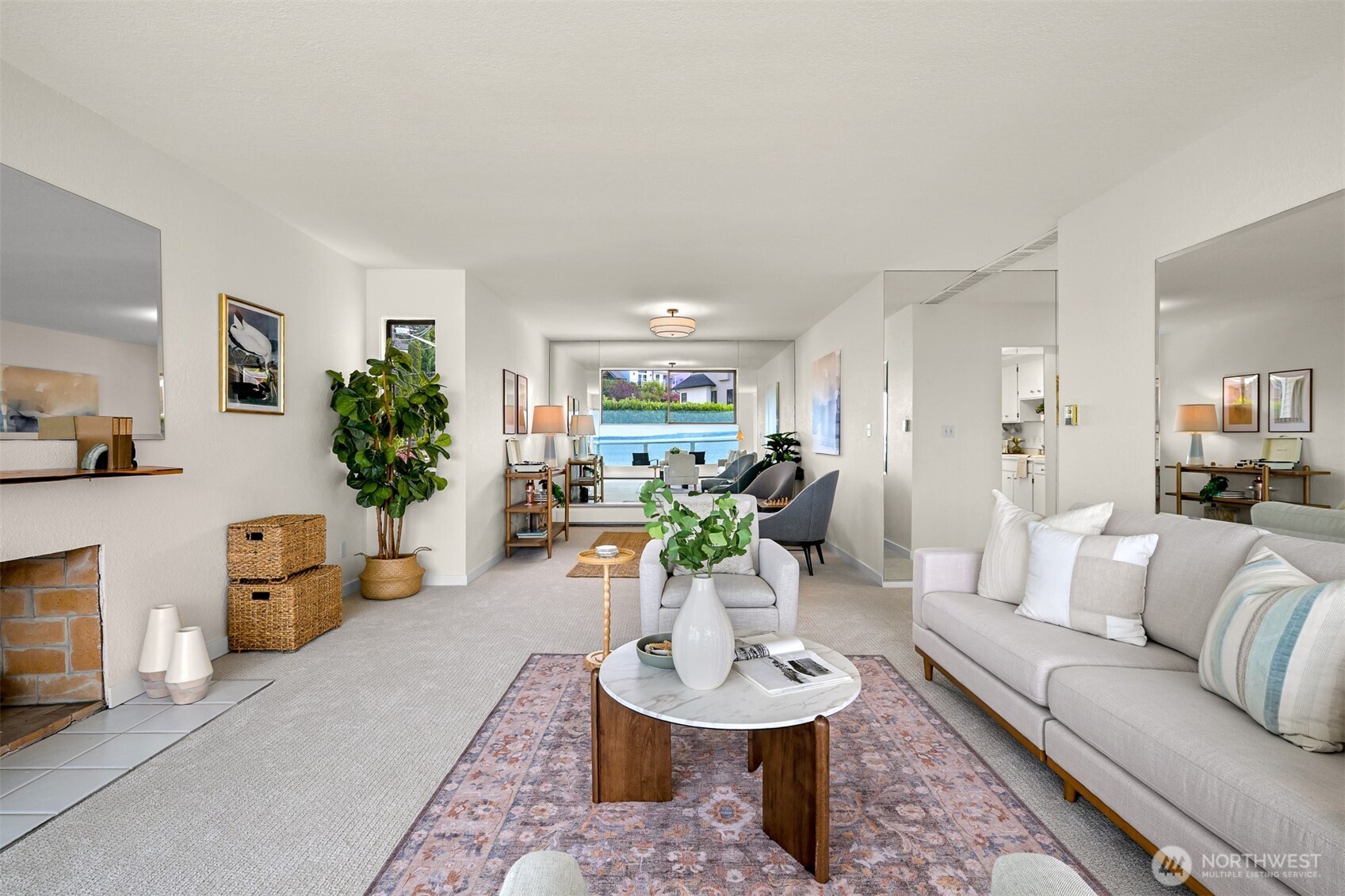 Furnished living room with a fireplace, patterned rug, and water visible through the windows.