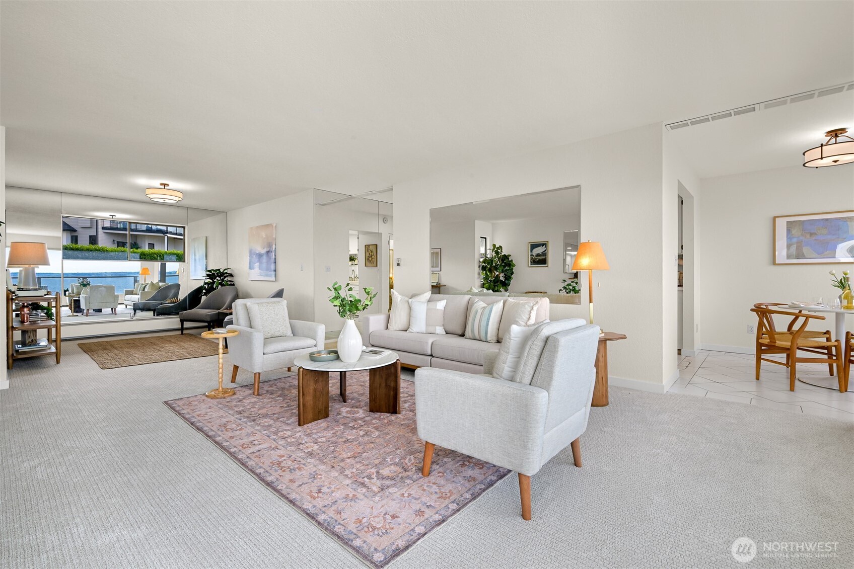 Staged living room with light gray seating, a patterned rug, and water views through large windows.