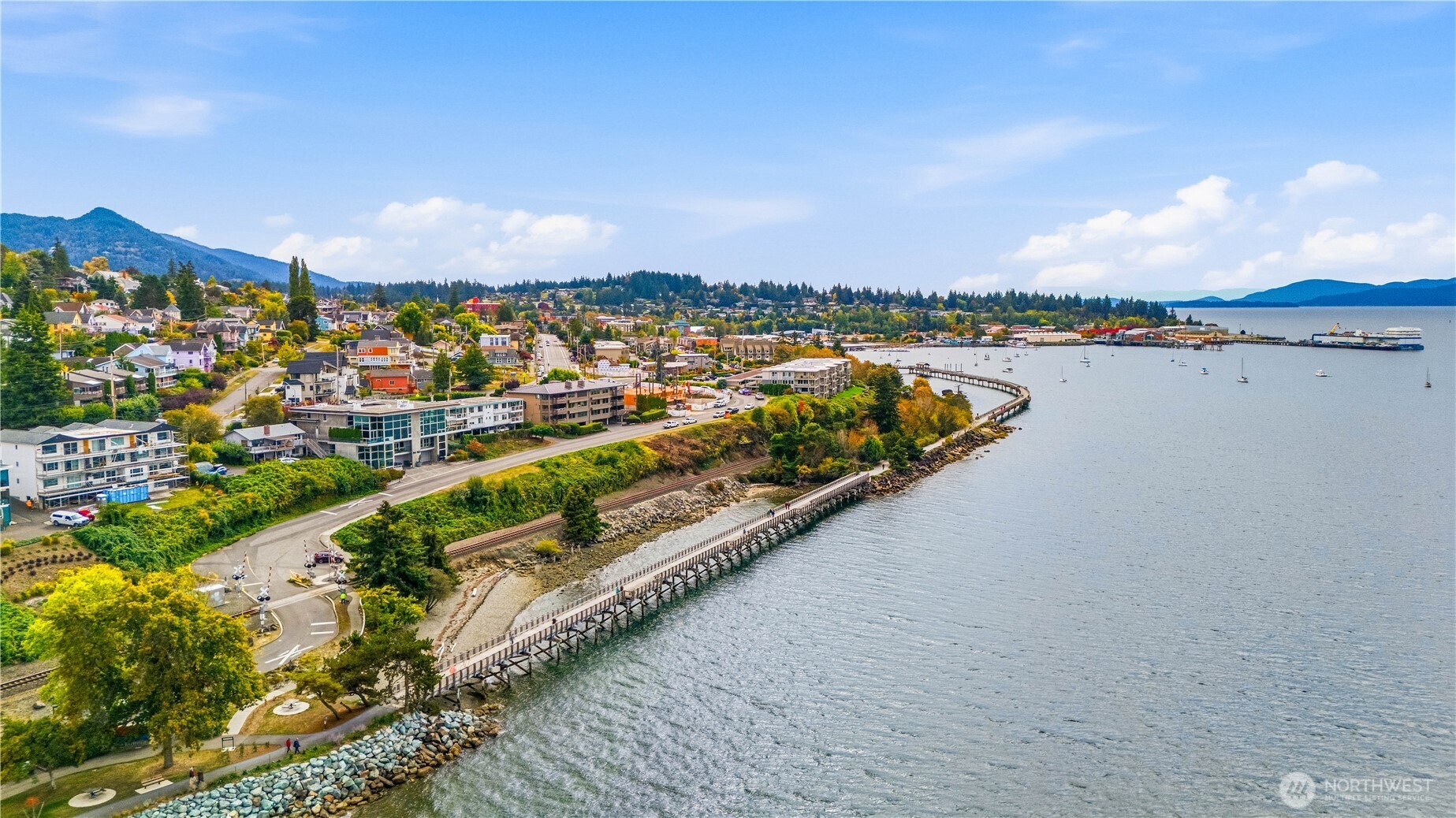 Aerial view of Bellingham’s waterfront, with a shoreline boardwalk, bay, and wooded hills.