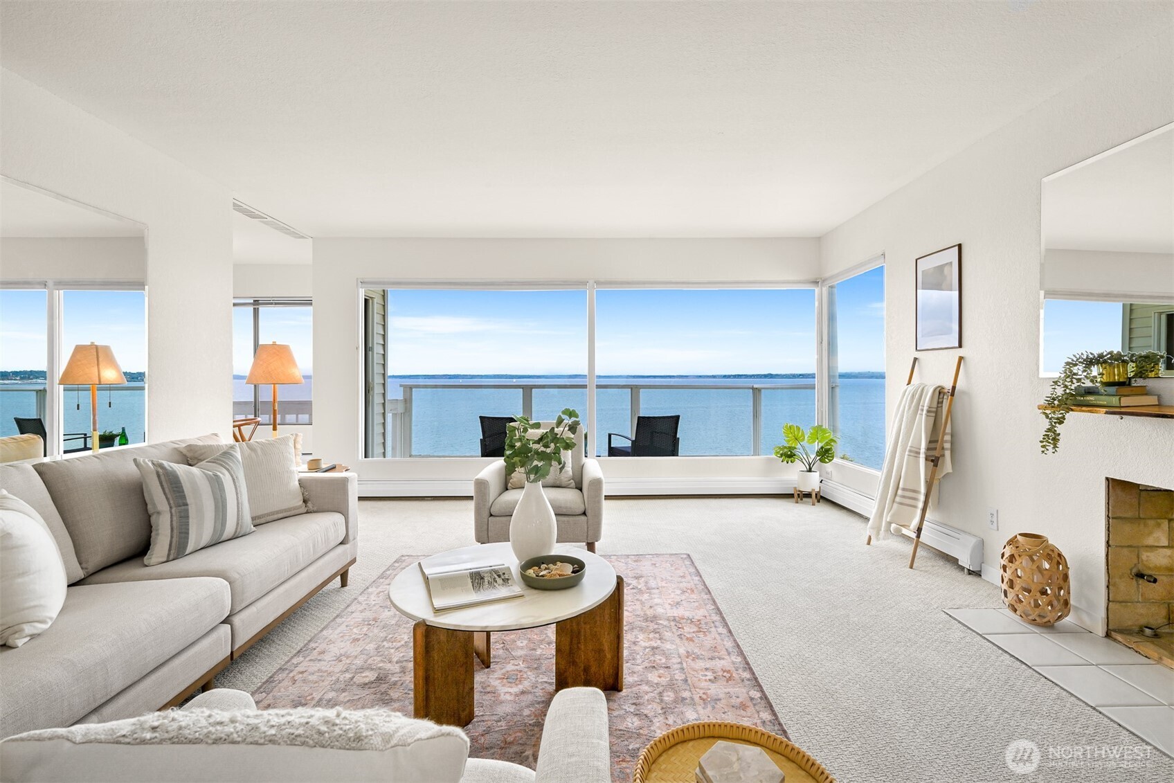 Waterfront living room with large windows, neutral furnishings, and a fireplace.