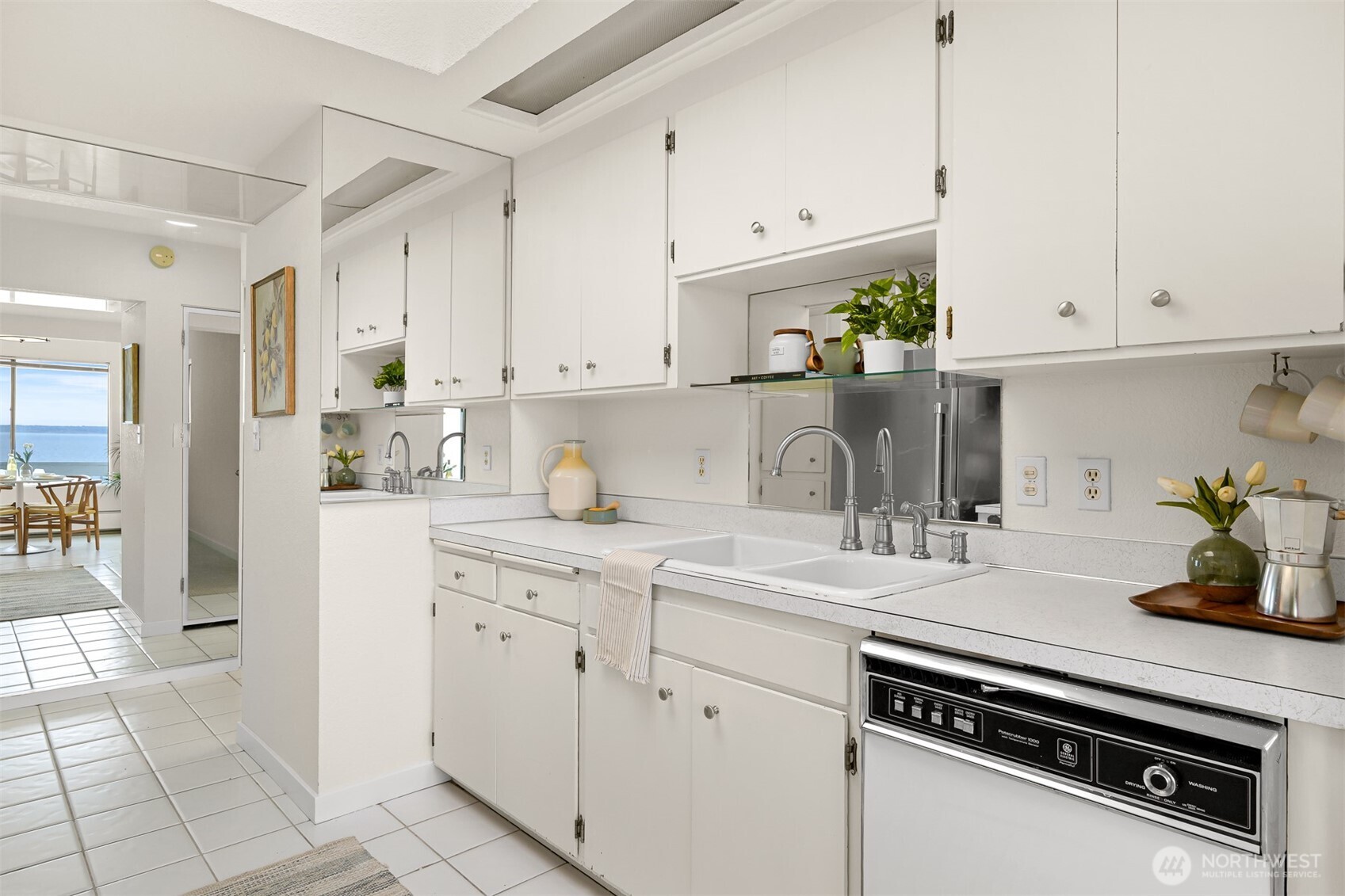 White condo kitchen with extensive cabinetry, a double-basin sink, and an adjoining dining area overlooking the water.