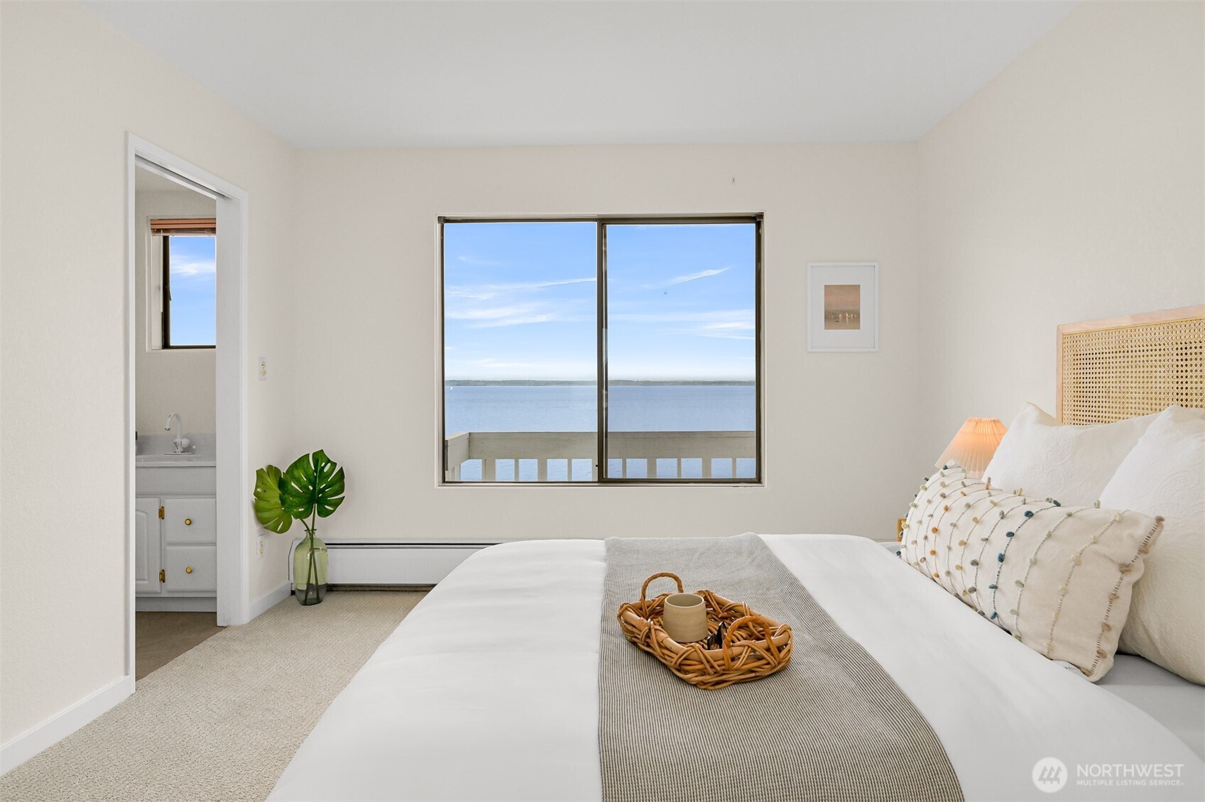 Bedroom with a large window overlooking calm water and a distant shoreline.