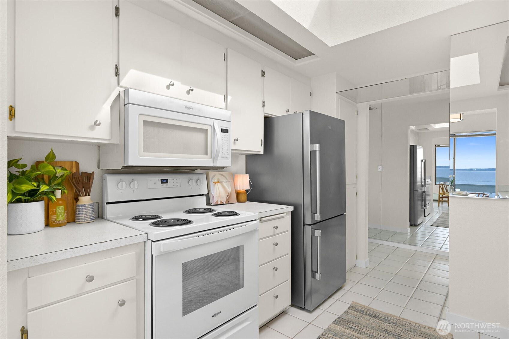 White kitchen with stainless steel refrigerator and a water view through the adjoining dining area.