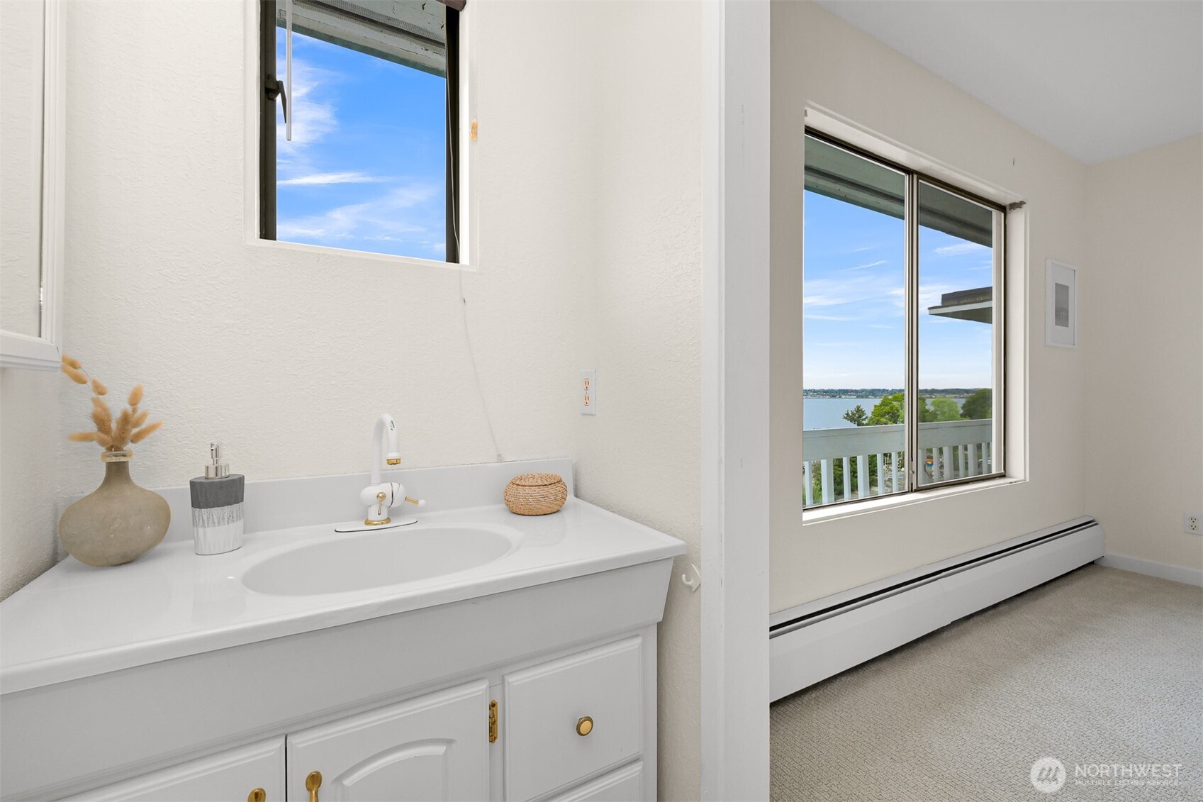 Bathroom vanity beside a carpeted room with a large window overlooking the water.