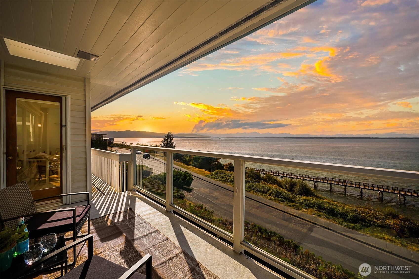 Furnished balcony overlooking the water and distant mountains at sunset.