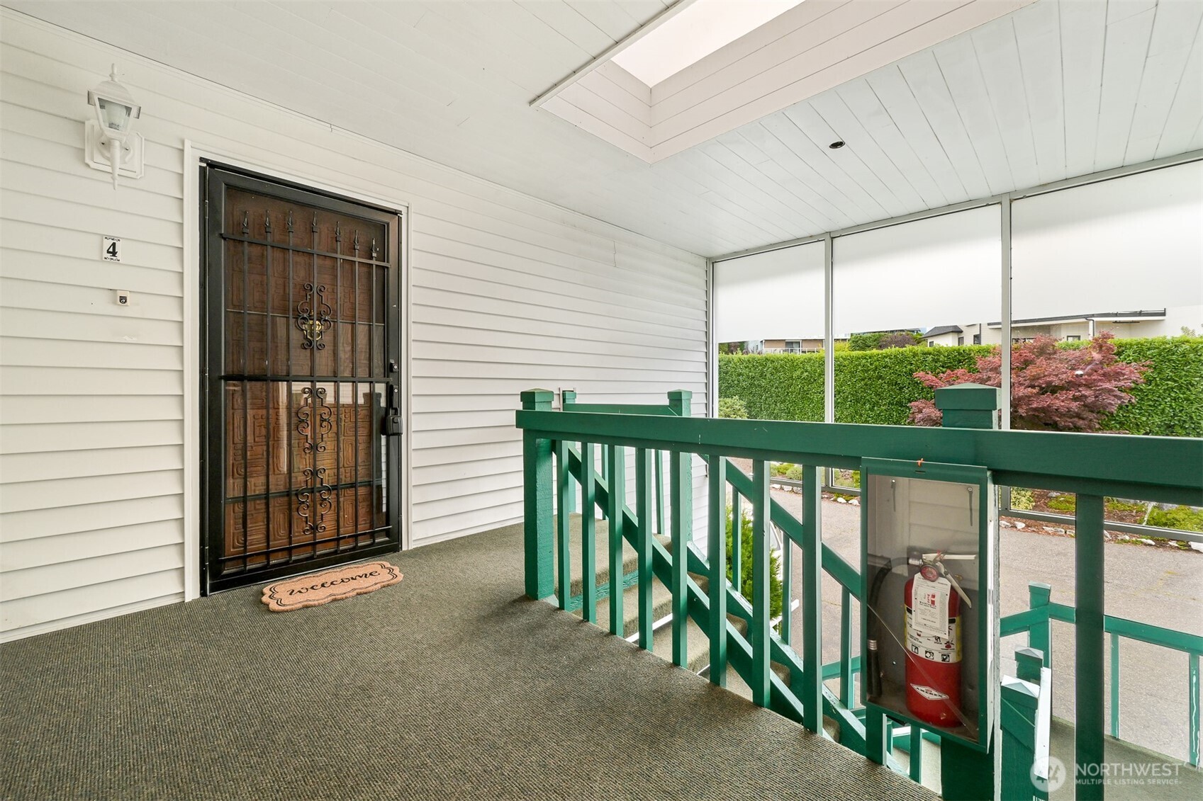 Covered condo entry porch with a decorative security door and green railings.