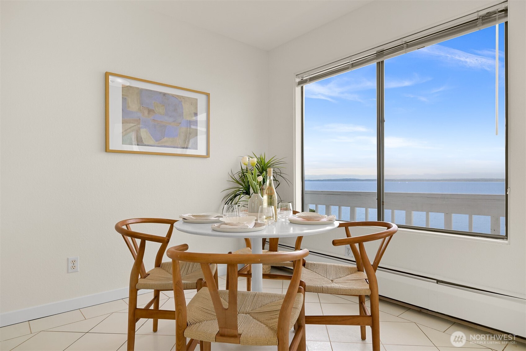 Dining area with a round table and wooden chairs beside a large window overlooking the water.