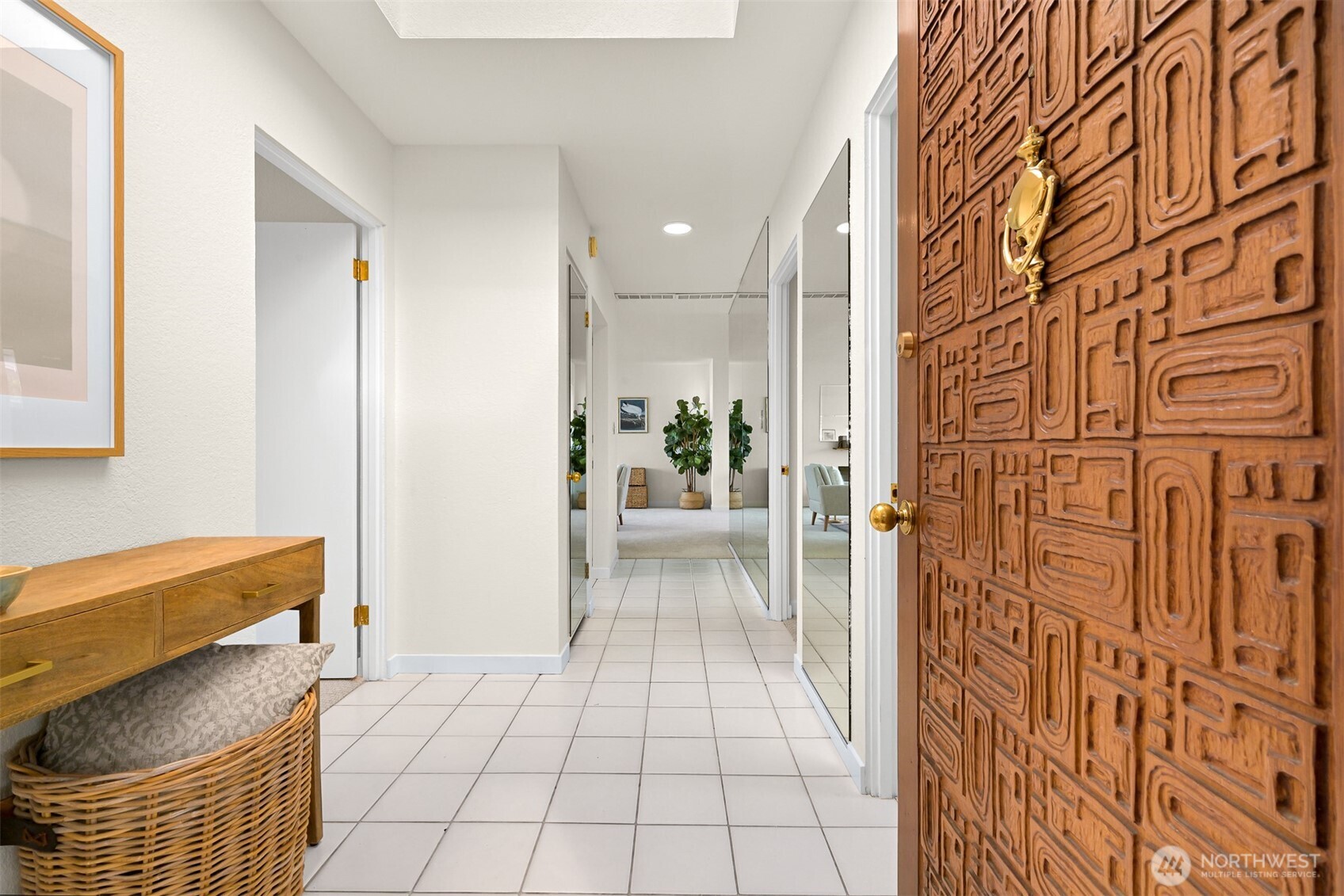 Tiled entry hallway with a carved wooden front door, console table, and mirrored closet doors.