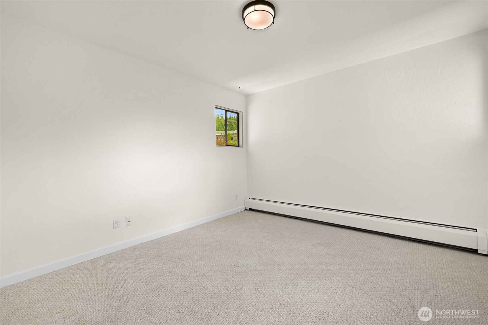 Empty bedroom with light gray carpet, a small window, and a long baseboard heater.
