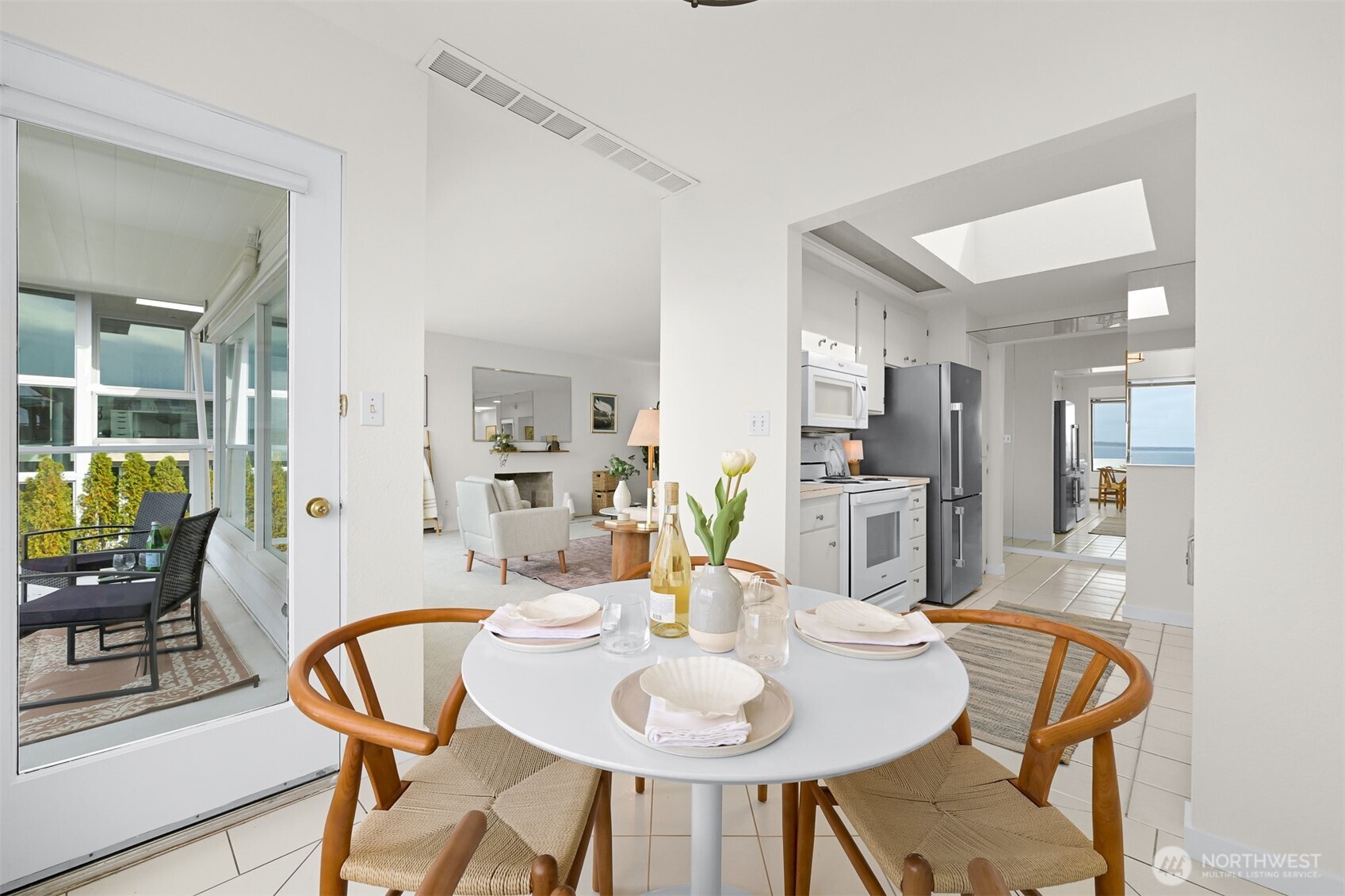 Staged dining area opens to a living room and kitchen, with a balcony and water views.