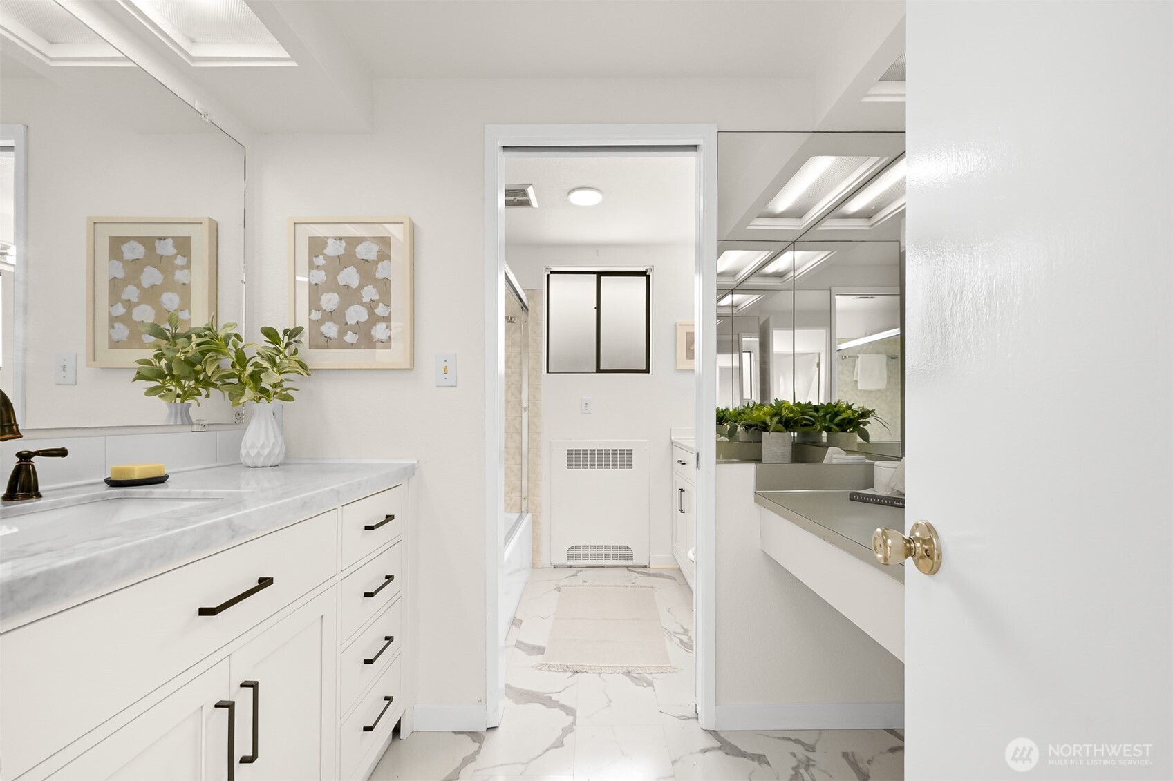 Bright bathroom with a marble-look vanity and floor, large mirrors, and potted plants.