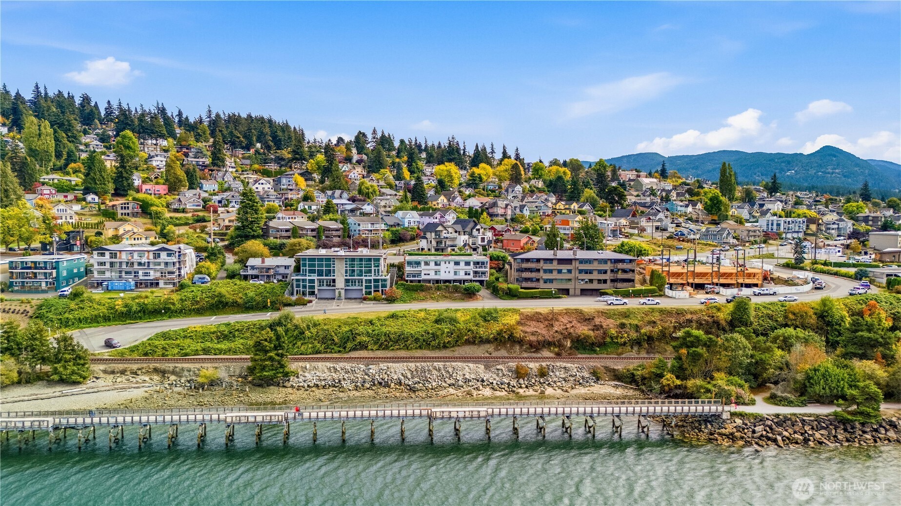 Aerial view of waterfront homes, a long pier, and wooded mountains.