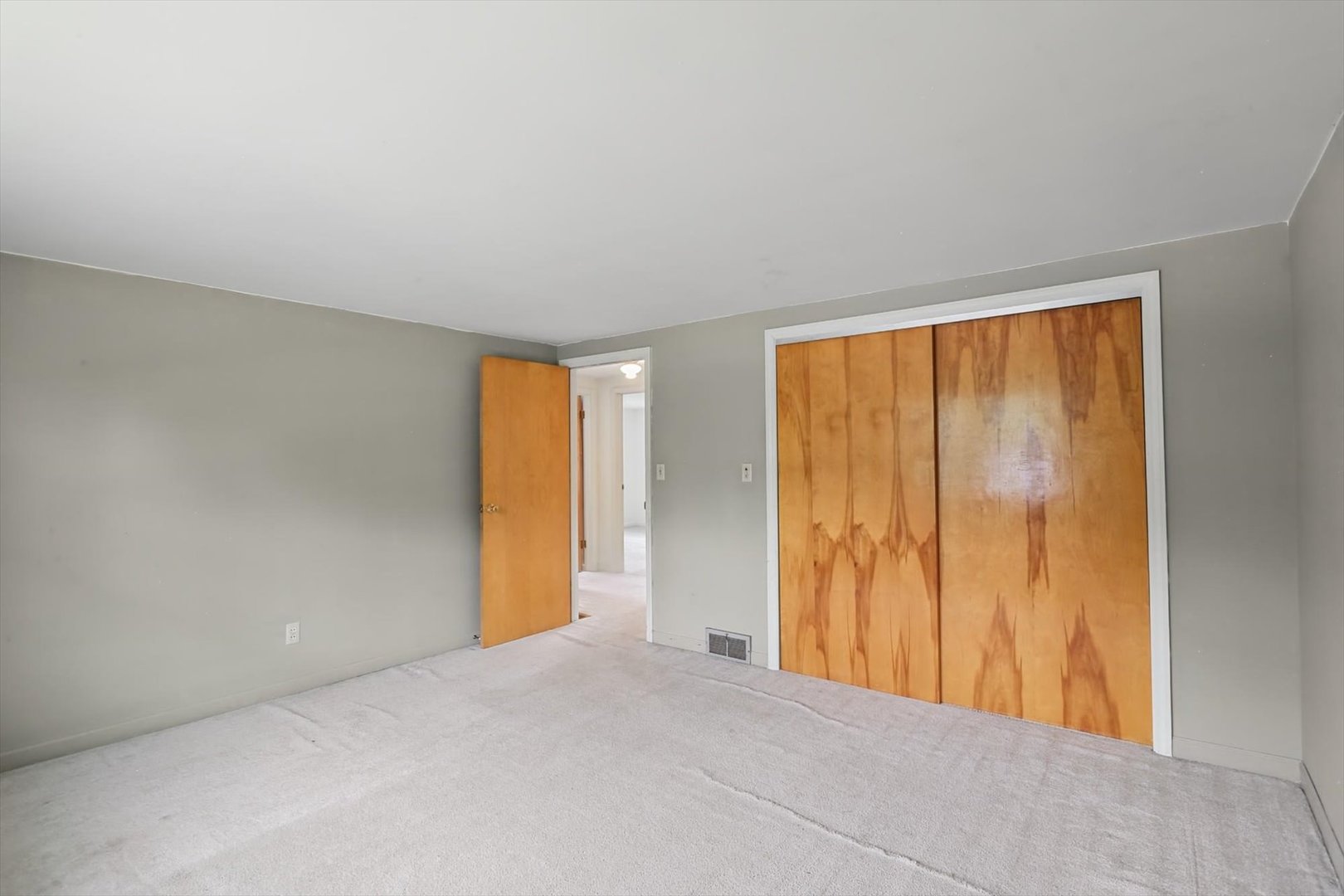 Empty bedroom with pale carpeting, gray walls, and wood-paneled sliding closet doors.