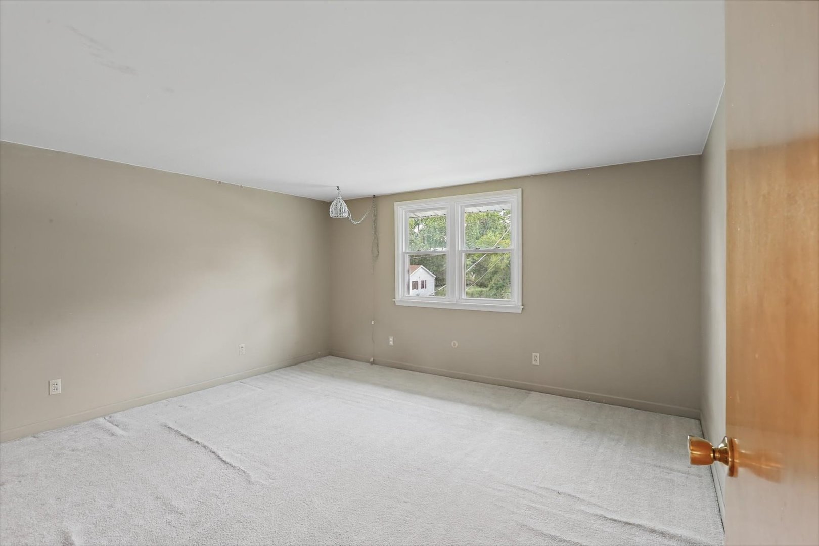 Empty bedroom with light carpet and a double window overlooking trees.