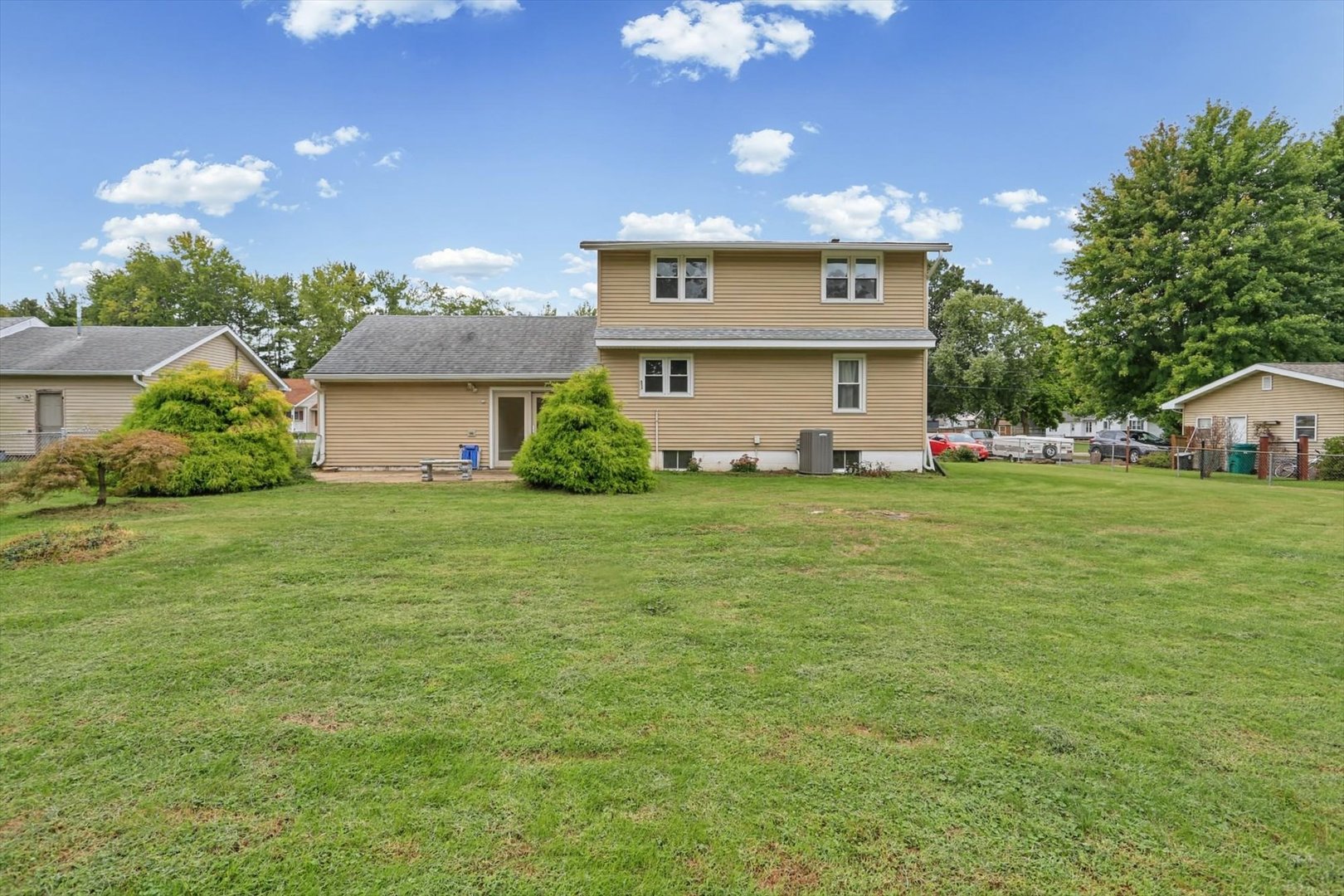 Rear exterior of a tan two-story home with a broad lawn and mature trees.