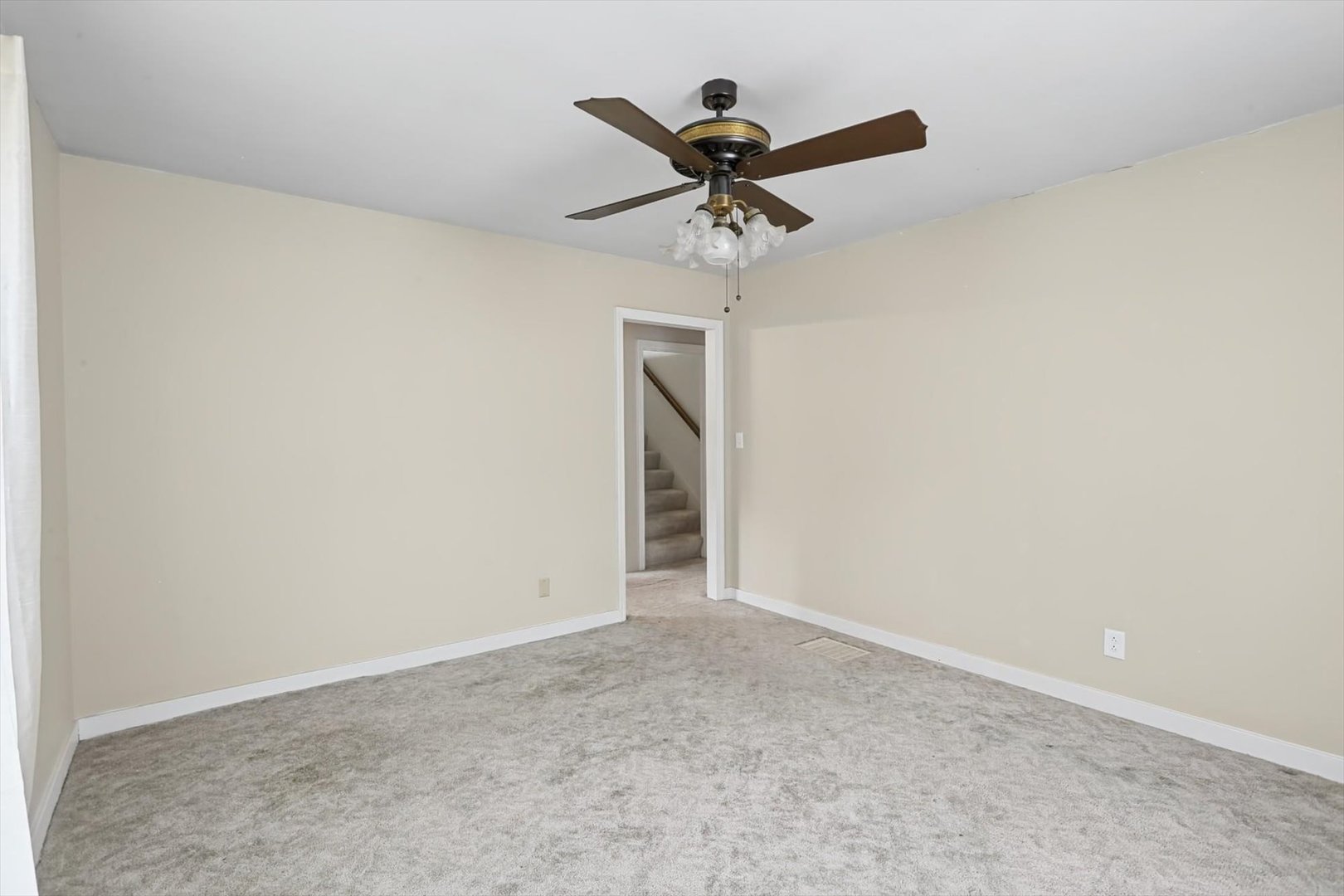 Empty carpeted room with a ceiling fan and doorway to a staircase.