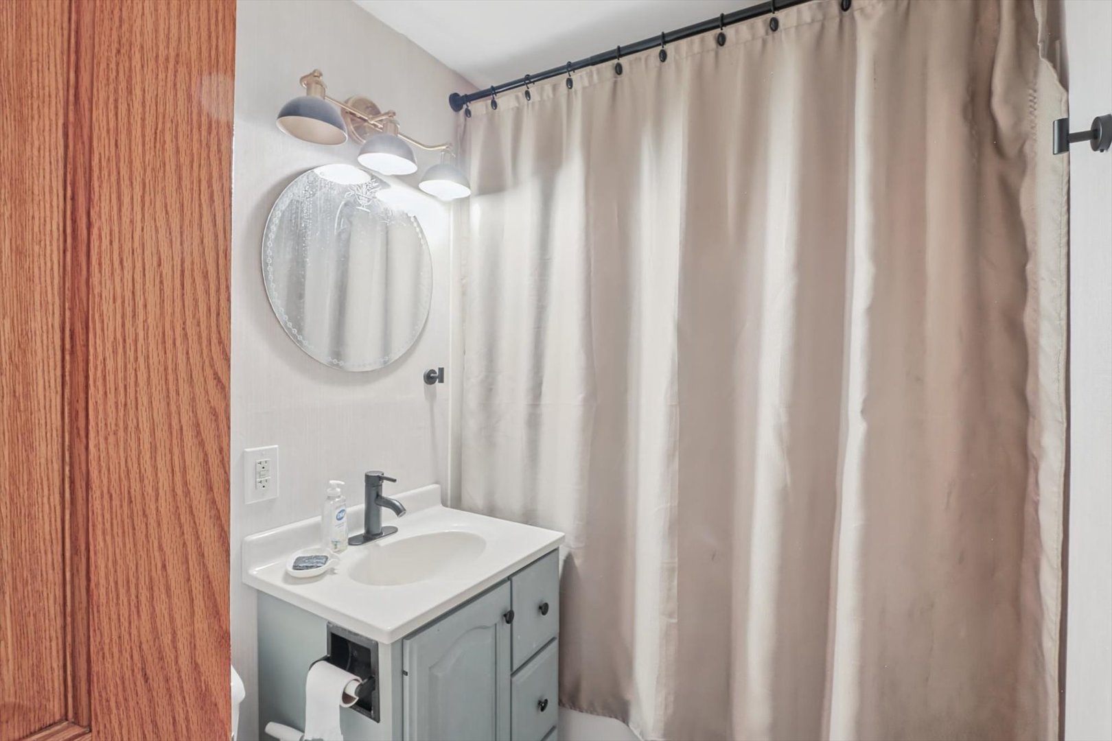 Bathroom with a light blue-gray vanity, round mirror, and beige shower curtain.