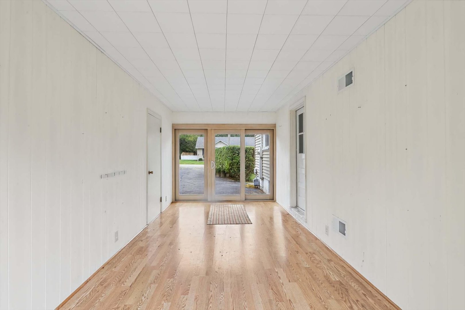 Empty sunroom with hardwood floors and sliding glass doors opening toward greenery.