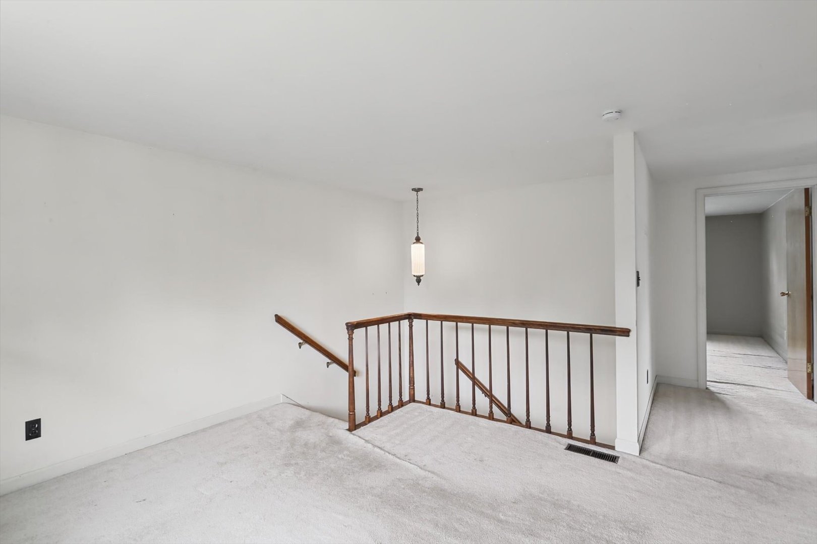 Carpeted upstairs landing with a dark wood stair railing and pendant light.