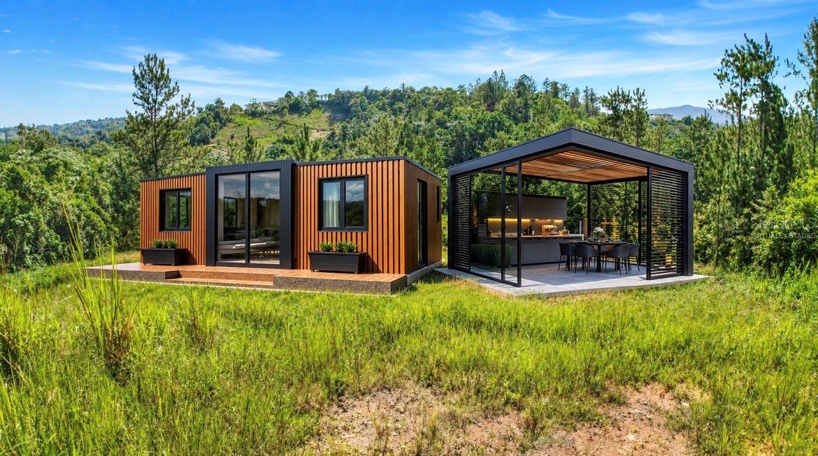 Modern home with orange-brown siding and a covered outdoor kitchen in a grassy, wooded setting.