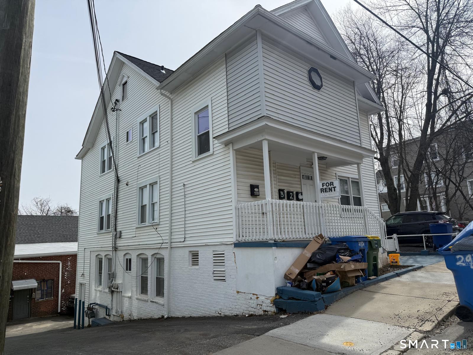 White multi-story house with a covered porch and a FOR RENT sign.