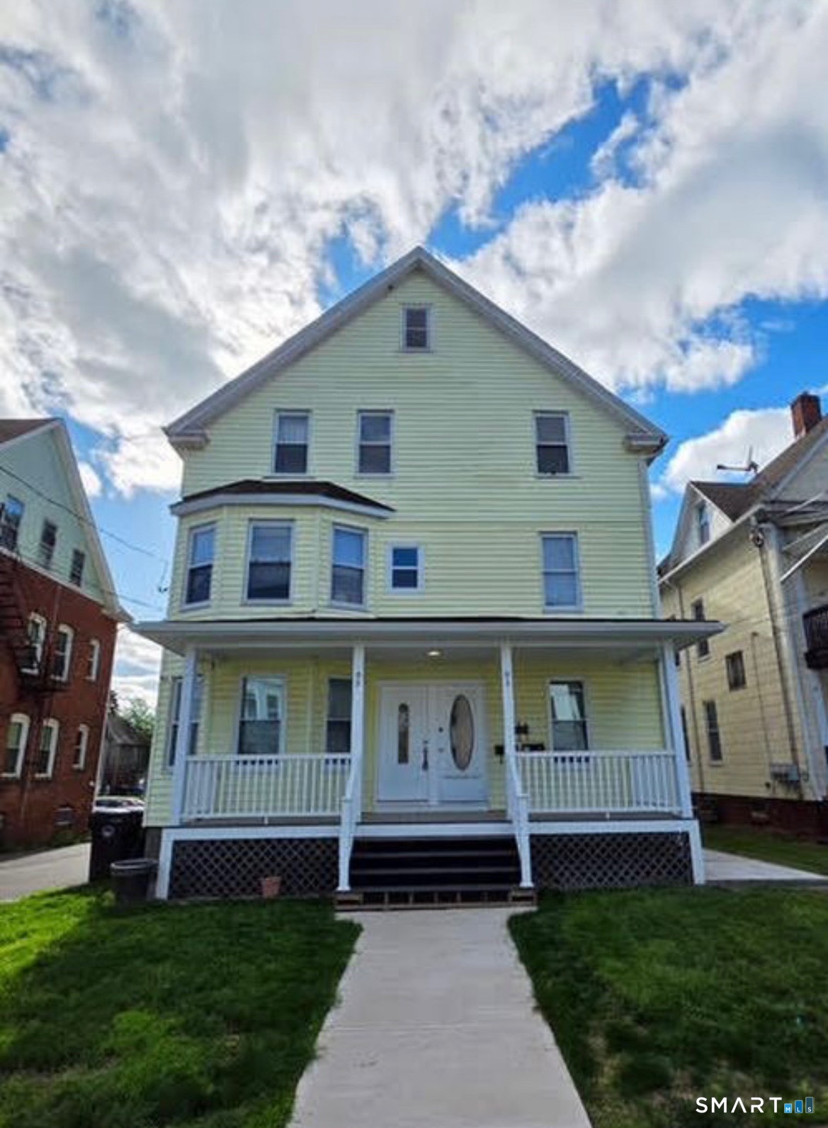 Pale green three-story house with a broad covered porch and a walkway across the lawn.