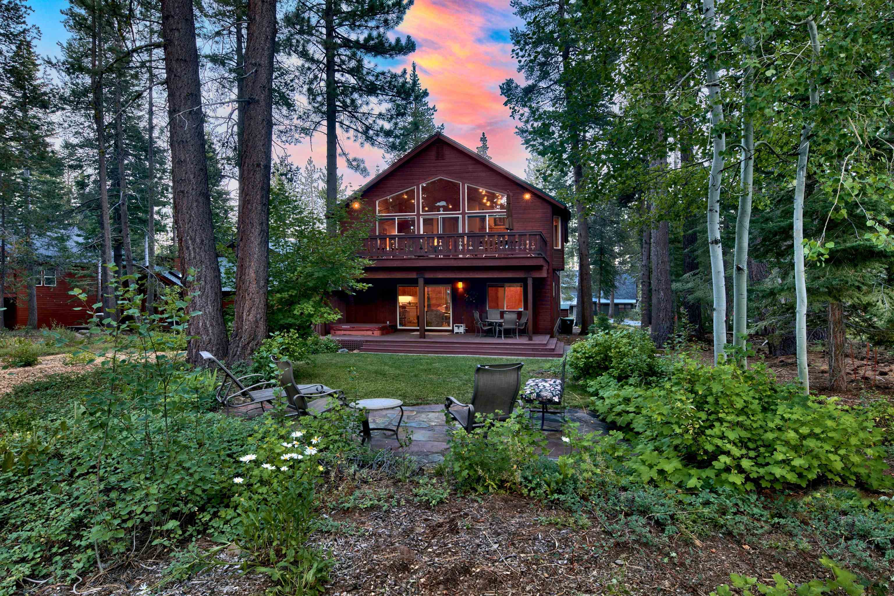 Wooded two-story home with a broad glazed gable, balcony, and garden patio at dusk.
