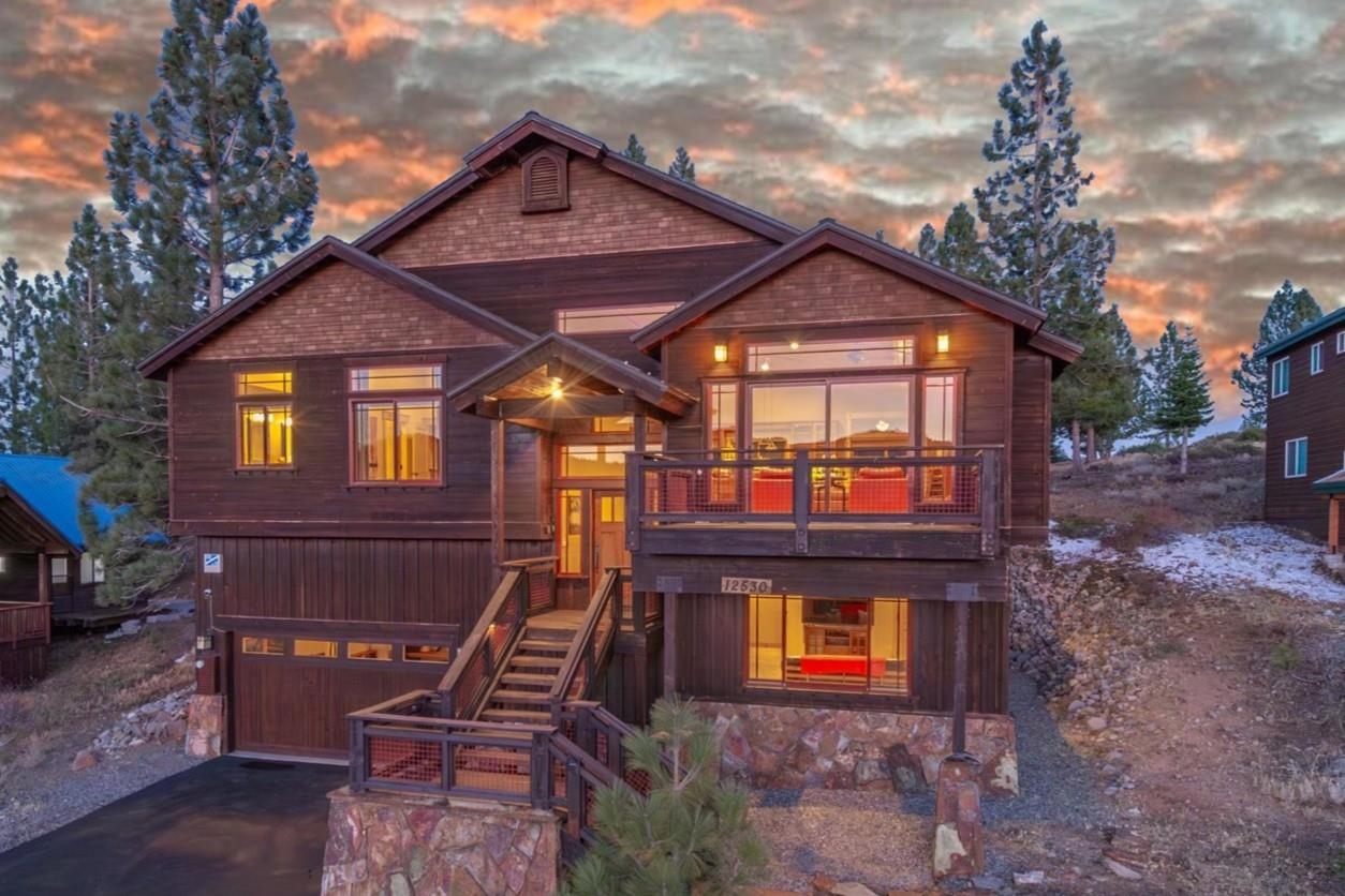 Multi-level wood mountain home with a balcony and glowing windows at dusk.
