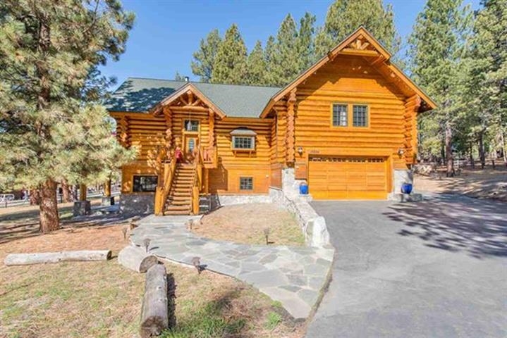 Log cabin with a two-car garage, front steps, and a curved stone walkway among pine trees.
