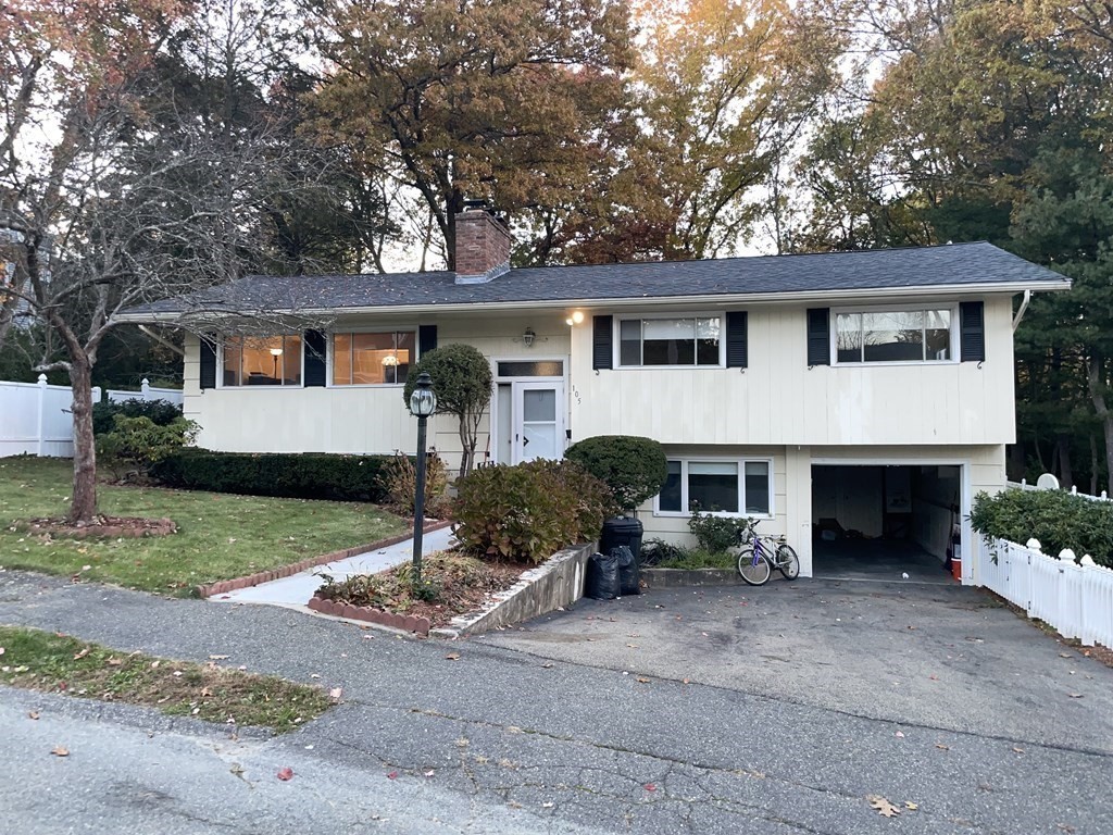 White split-level house with black shutters, an attached garage, and autumn trees.
