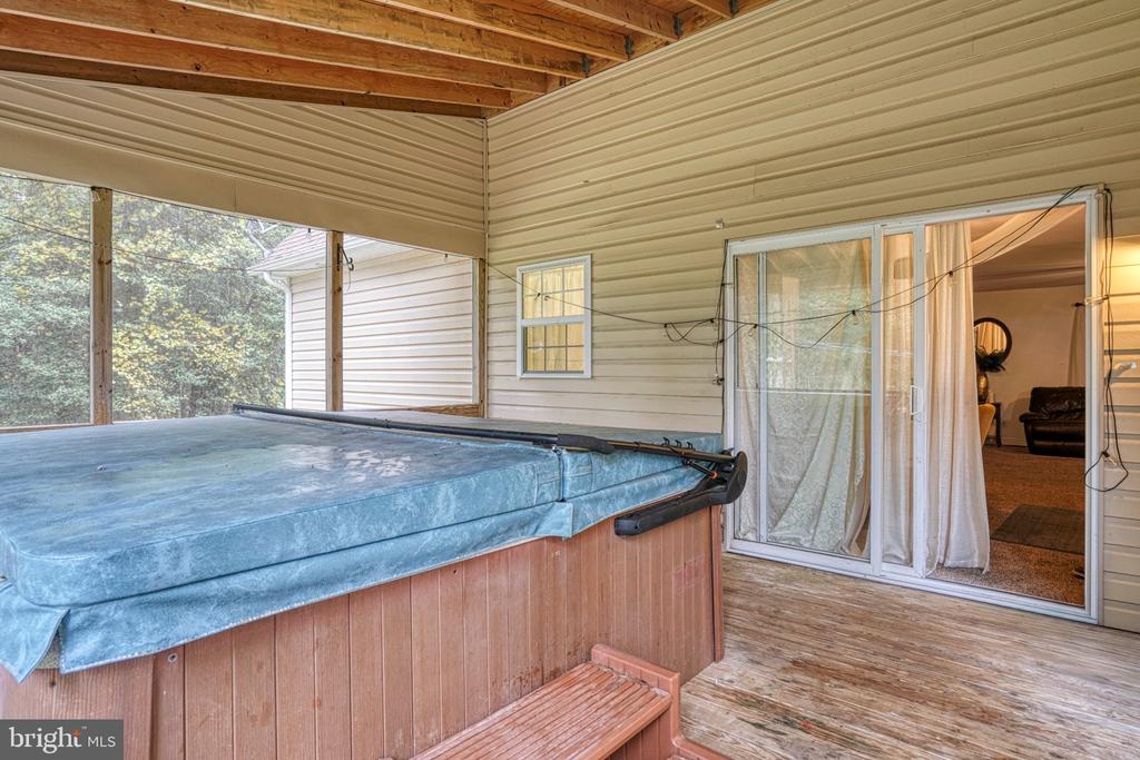 Covered porch with a large hot tub beside a sliding glass door.