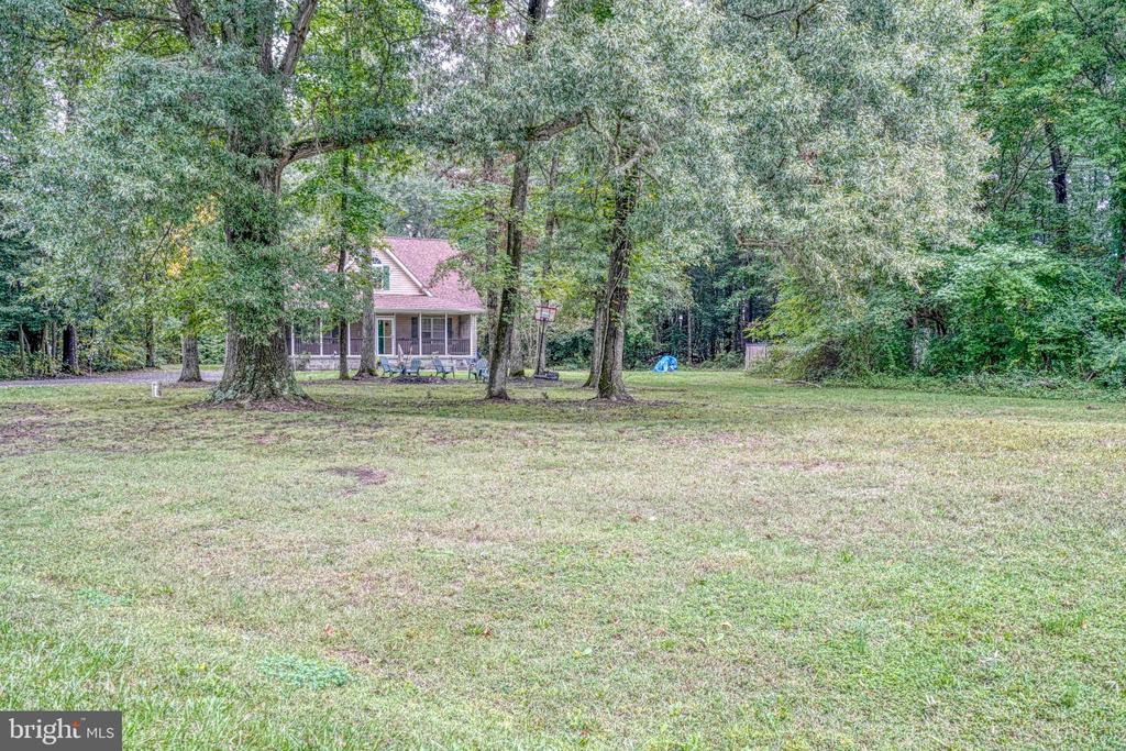 House with a covered porch set among mature trees beside a broad grassy lawn.