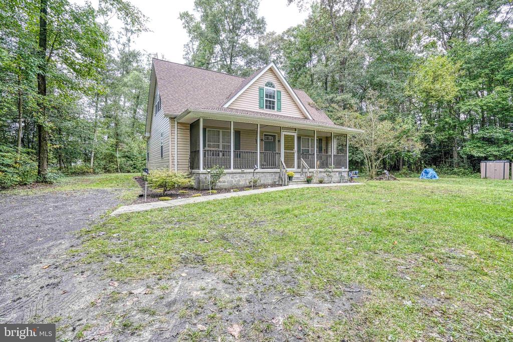 Beige gabled house with a screened porch, stone foundation, and wooded lawn.
