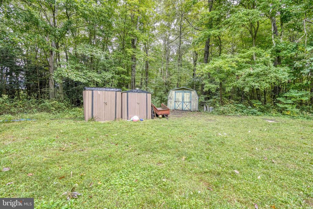 Grassy backyard with three storage sheds at the edge of a wooded lot.