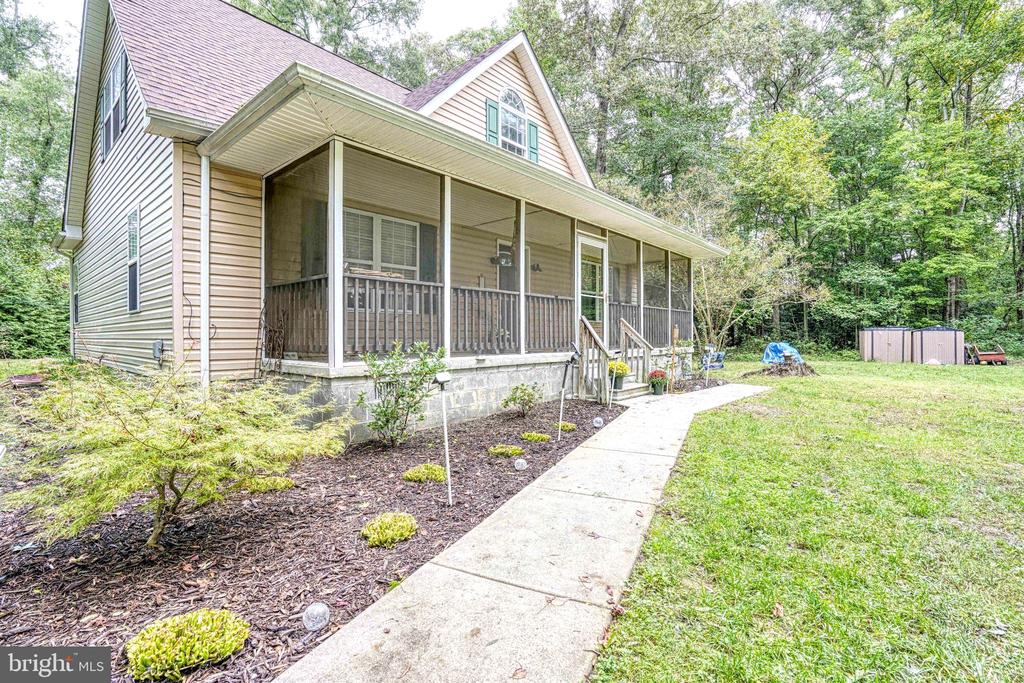 Tan two-story house with a long screened porch, concrete walkway, and wooded lawn.