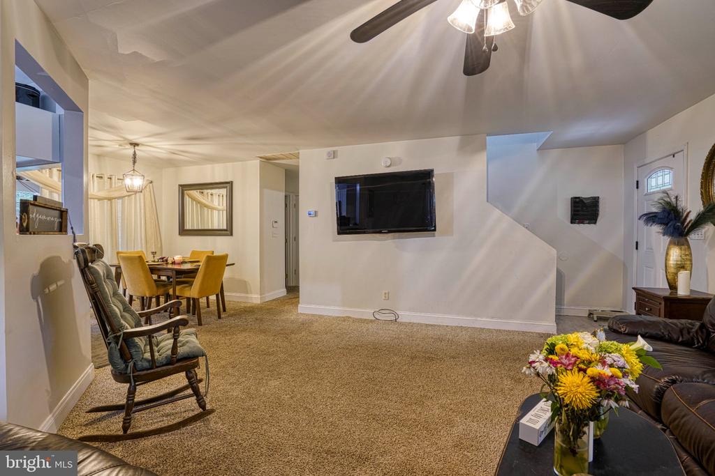 Living room with beige carpet, leather seating, and an adjoining dining area with yellow chairs.