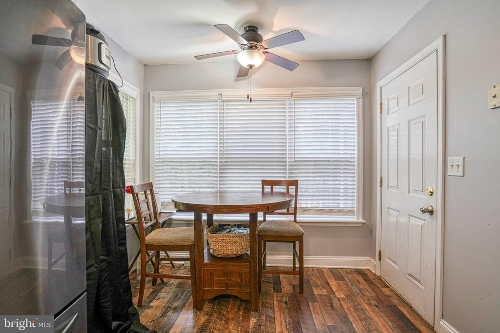 Dining nook with a round wooden table, wide windows with blinds, and a ceiling fan.