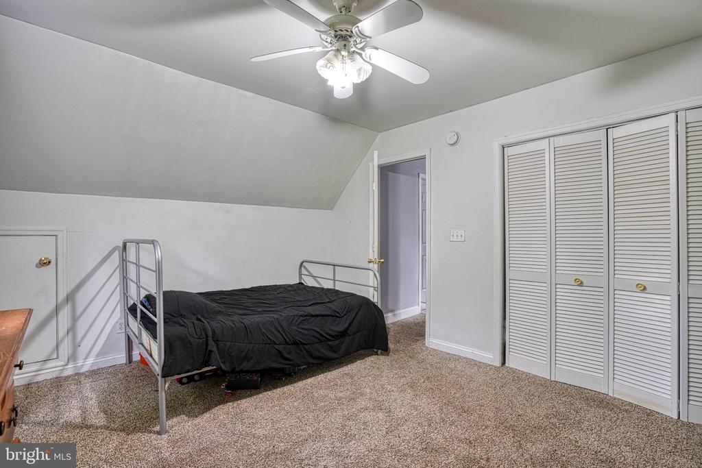 Upstairs bedroom with a sloped ceiling, black-bedded metal bed, beige carpet, and louvered closet doors.
