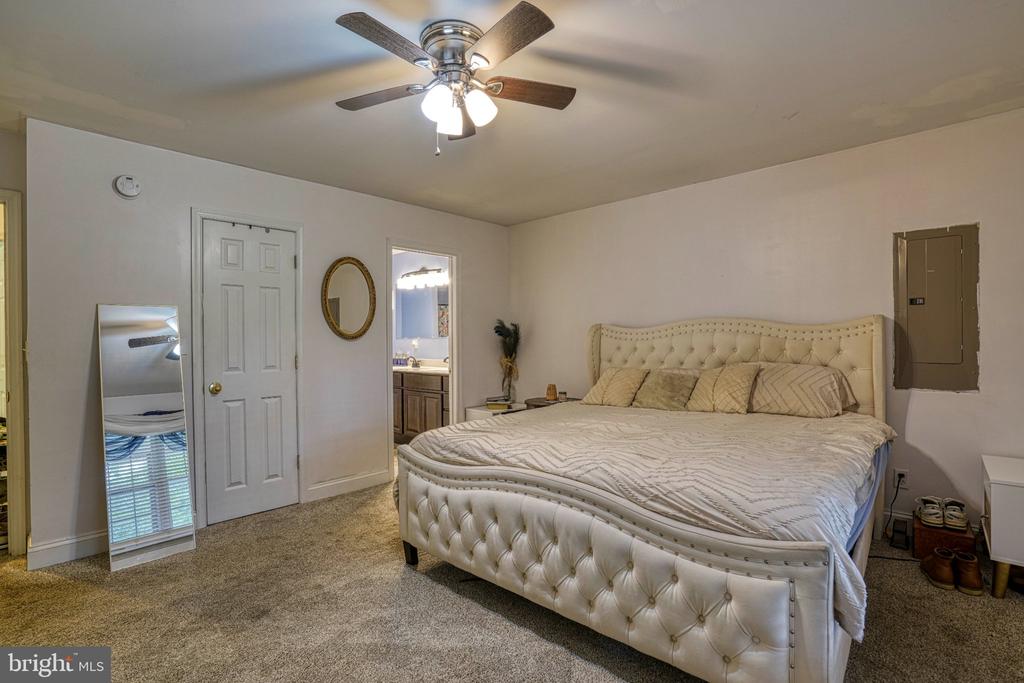 Bedroom with a large cream tufted bed, beige carpet, and ceiling fan with lights.