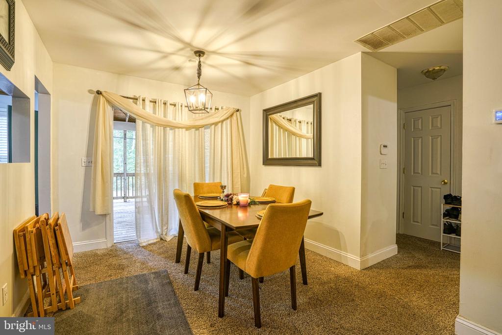Dining room with a wooden table, upholstered chairs, hanging lantern, and curtained doors to a deck.