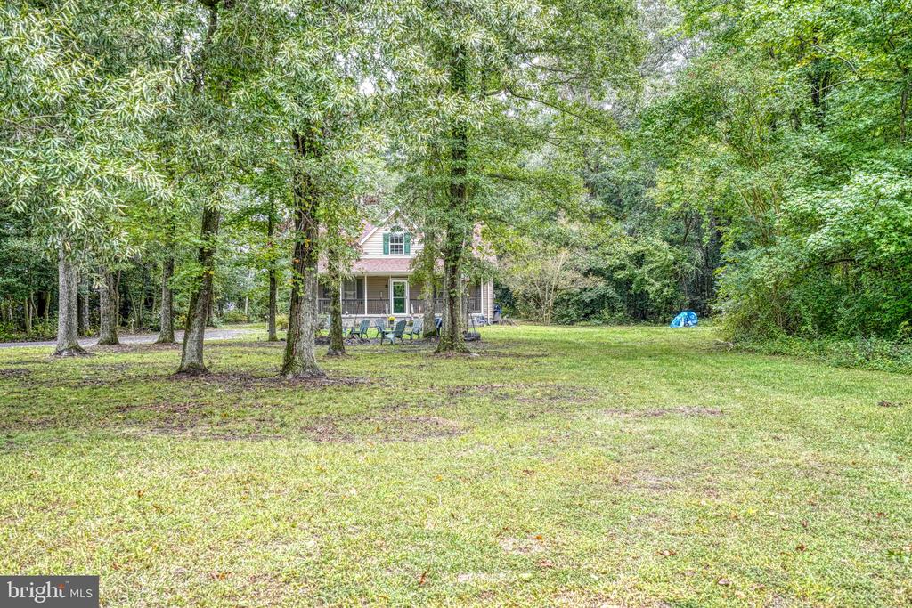 House partly hidden among mature trees beyond a broad lawn, with chairs on its covered porch.