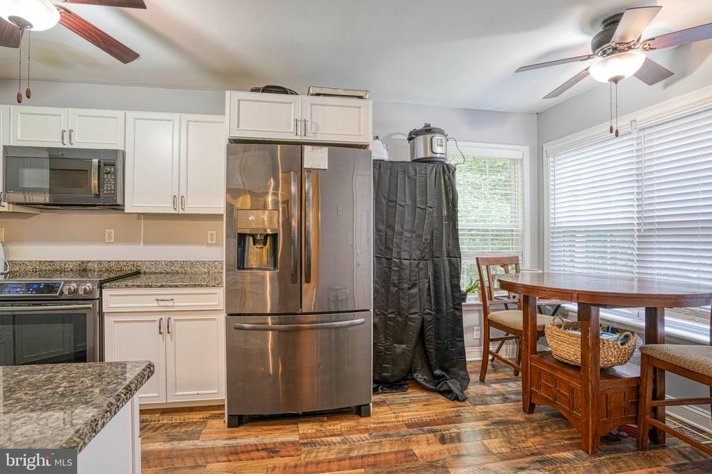 Kitchen with white cabinetry, stainless steel appliances, granite counters, and a dining table beside large windows.