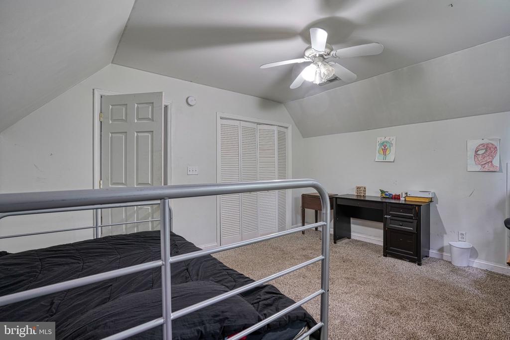Upstairs bedroom with a metal bunk bed, sloped ceiling, beige carpet, and dark desk.