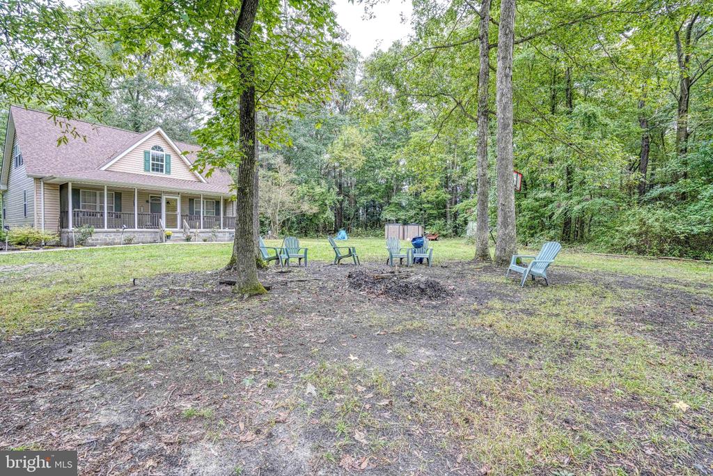 Wooded backyard with outdoor chairs, mature trees, and a beige house with a covered porch.