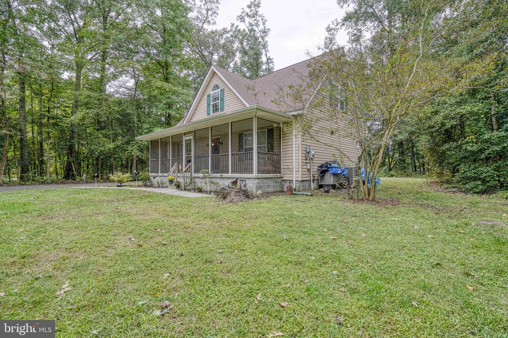 Beige house with a covered porch on a grassy, tree-lined lot.