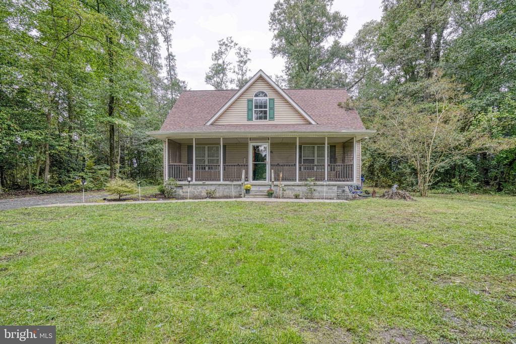 Front exterior of a tan house with a covered porch, upper dormer, and broad lawn.
