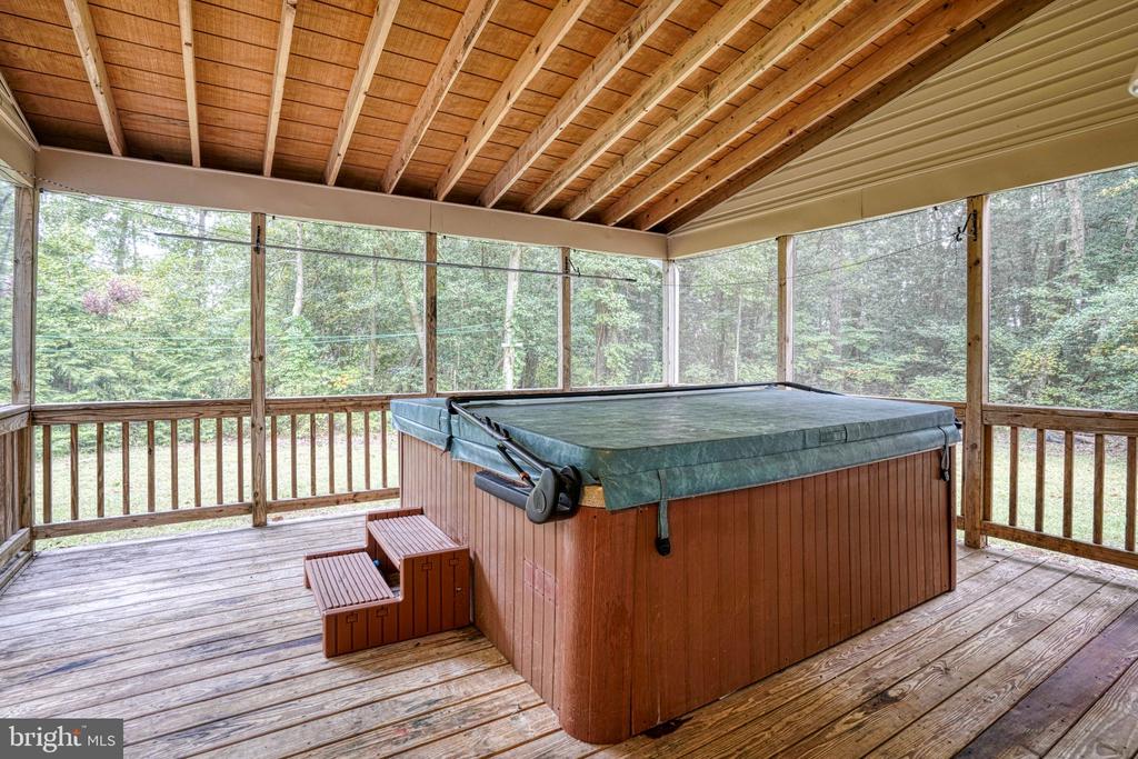 Screened porch with a large hot tub, wooden decking, and exposed ceiling beams.