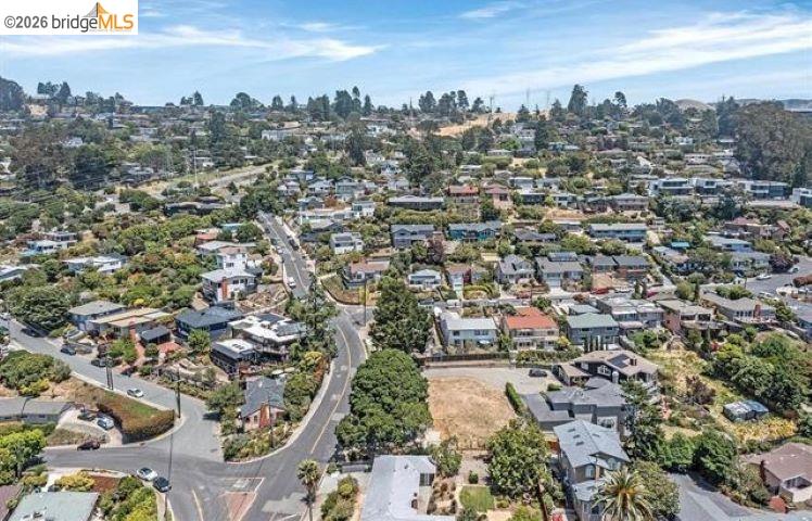 Aerial view of a leafy neighborhood with detached homes, winding streets, and low hills in the distance.