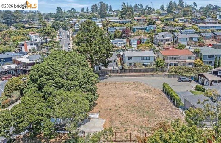 Aerial view of a vacant residential lot bordered by trees and homes.